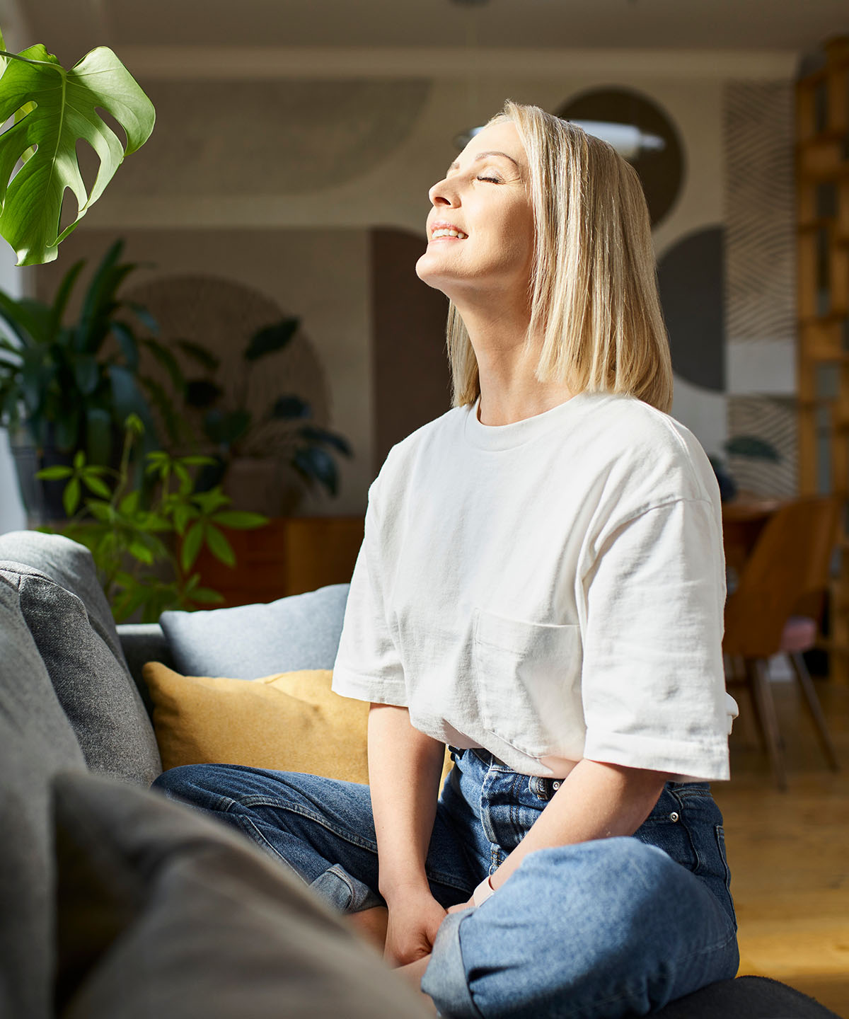 Woman sitting on a couch with eyes closed, breathing in a moment of peace
